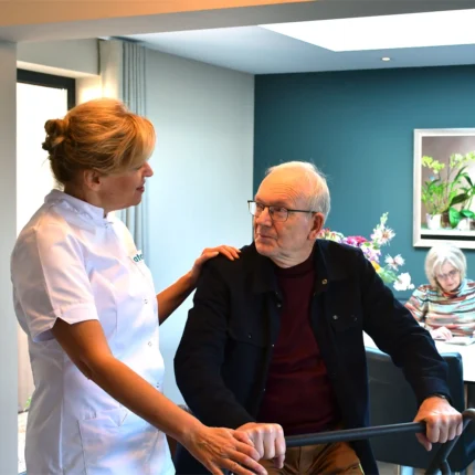 MoverFlexi. Man zit op Mover Flexi, verzorger staat naast hem met haar hand op zijn schouder