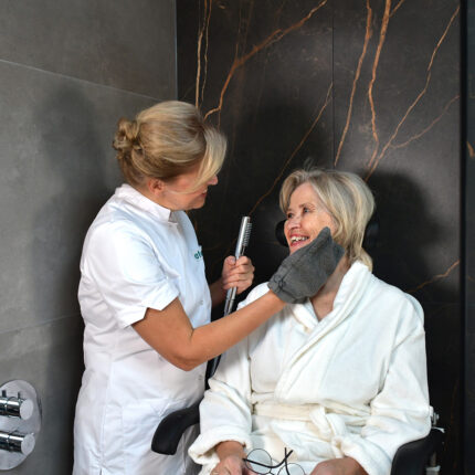 WeCare Family. Douche en toilet zorghulpmiddelen. Op de foto zie je zorgvrager op een douche-toiletstoel. Een ergonomisch zorghulpmiddel voor zorggever die er naast staat.