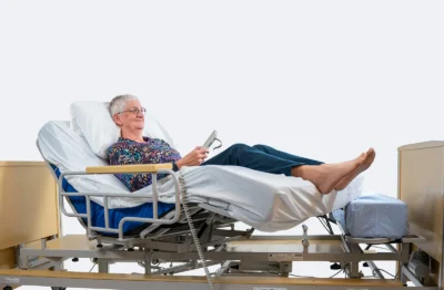 Comfortabel uit bed mogelijk door Freedom Easy Up. Vrouw zit met afstandsbediening in handen en gaat zelfstandig uit bed.