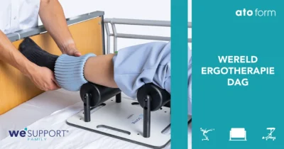 Op de afbeelding is het voeteneind van een bed te zien. Iemand steunt met haar been op Doffie terwijl een verzorger steunkousen aantrekt met behulp van de rollers op de Doffie. Daarnaast staat geschreven Wereld Ergotherapiedag 2025 en product icoontjes van Soqqie, Doffie en Change. Op de foto zelf staat ook het logo van WeSupport Family en van ATO FORM.