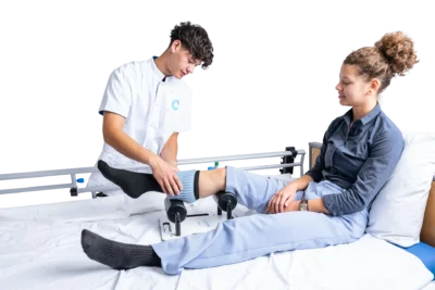 Verzorger doet met de Doffie een steunkous aan bij een jonge vrouw die in een zorgbed zit.