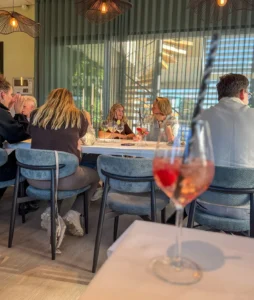 Op de voorgrond een glas met een roze mocktail en een zwart-wit gestreept rietje. Daarachter zitten collega's van ATO met elkaar te praten aan een lange, gedekte tafel met een wit tafelkleed, glazen en kaarsen.