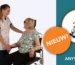 Links een lachende zorgverlener in een wit uniform die de hand vasthoudt van een oudere vrouw met blond haar en een bril. De vrouw zit in een stoel met hoofdsteun en zwarte armleuningen. Rechts op een teal vlak een productfoto van Anytoilet L op wielen, met een oranje sticker met de tekst nieuw.